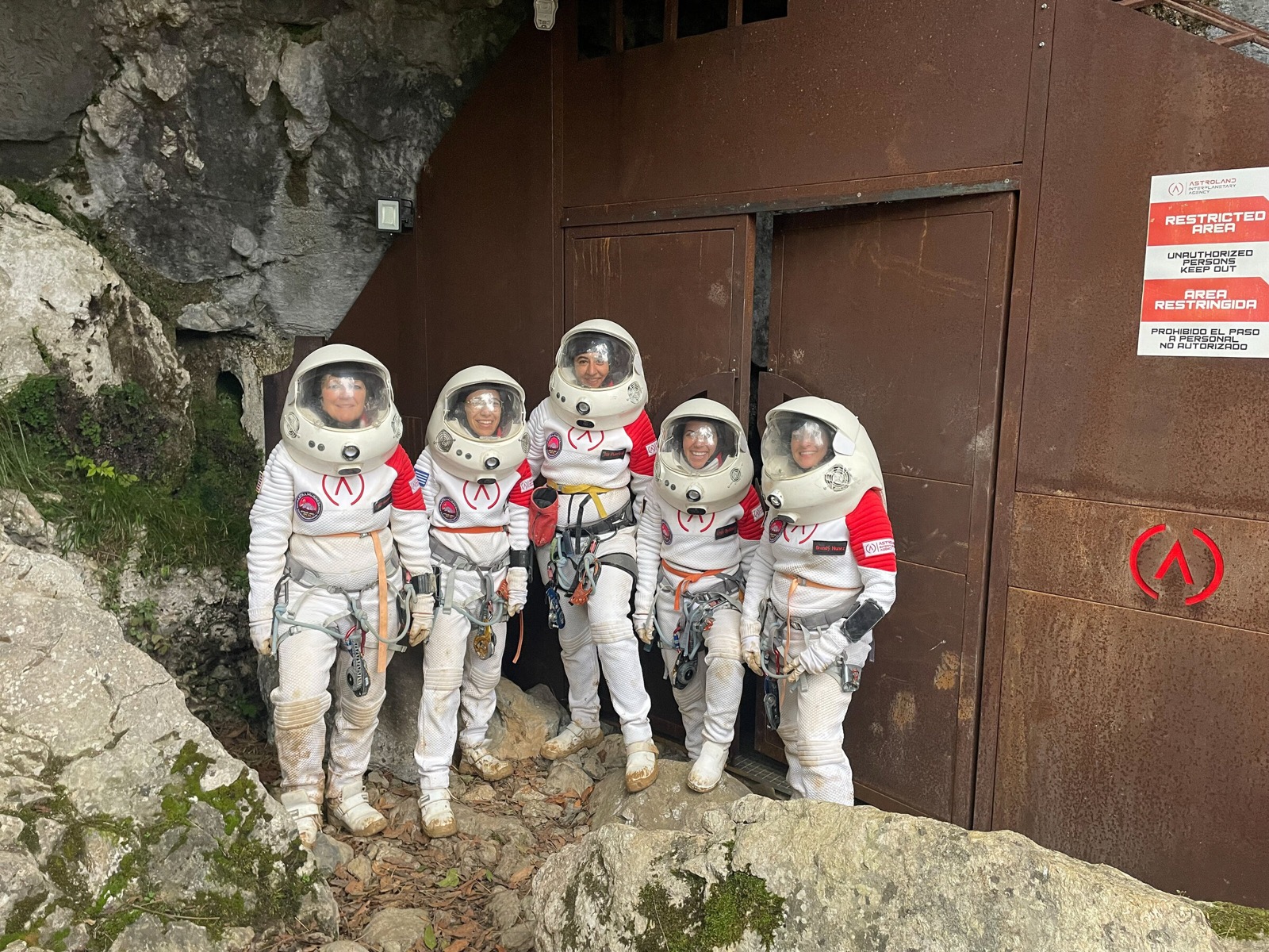 Crew in white analog spacesuits outside a habitat airlock